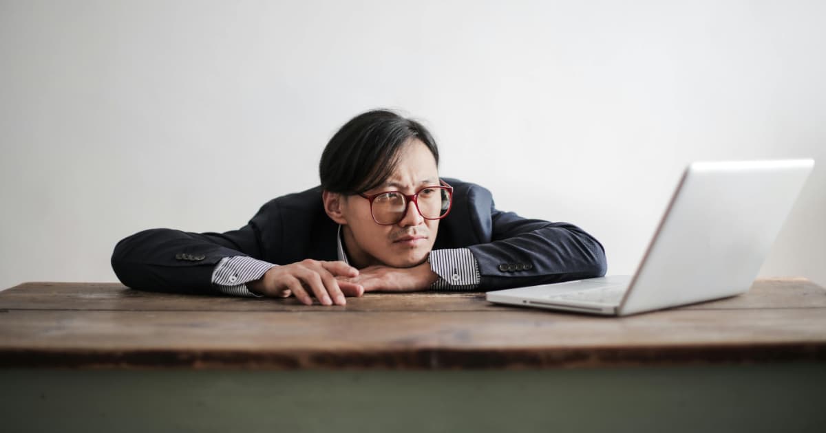 Frustrated freelancer resting head on desk staring at laptop waiting for overdue invoice payment