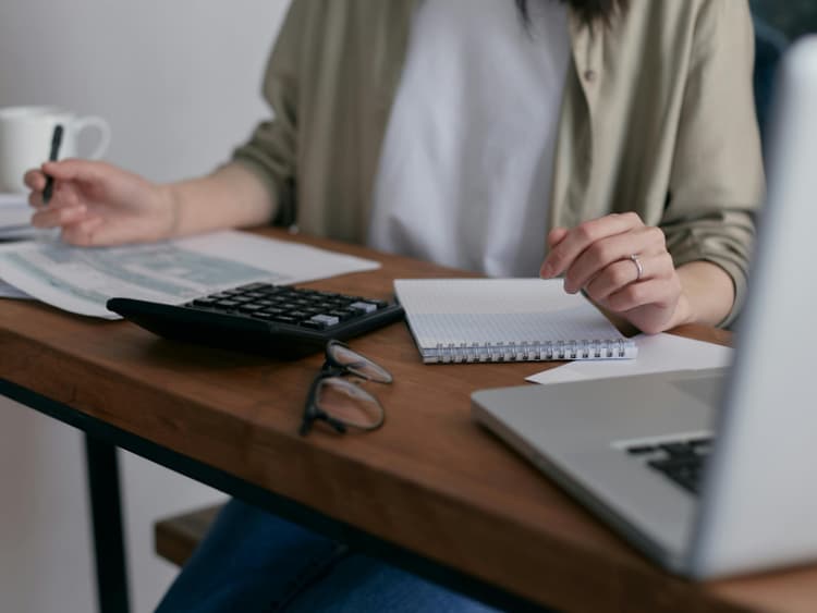 Freelancer at desk with calculator, notebook, and laptop for invoice calculations