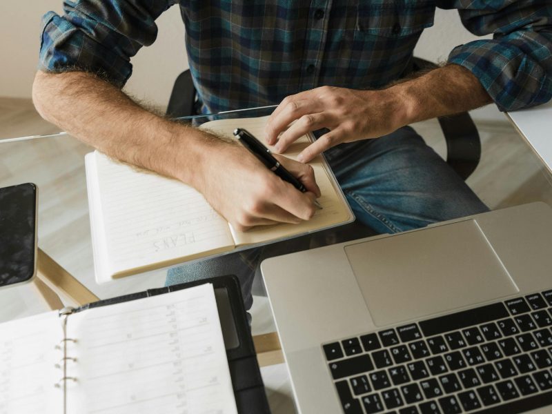 Freelancer writing plans in a notebook next to laptop